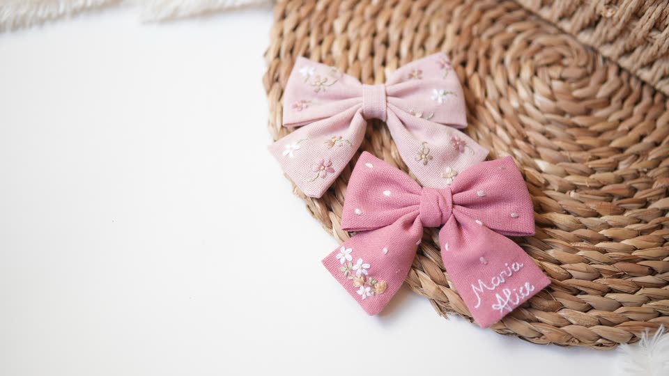 Dois laços rosa bordados com flores e o nome Maria Alice